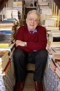Der Autor sitzt auf seiner Treppe im Haus, rechts und links sind Bücher gestapelt